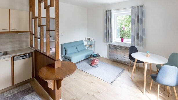 A modern kitchen with wooden cabinets, a built-in dishwasher, and a dining area with a round wooden table and two chairs. - Gailtaler Apartment at an Excursion Location (Kotschach-Mauthen)