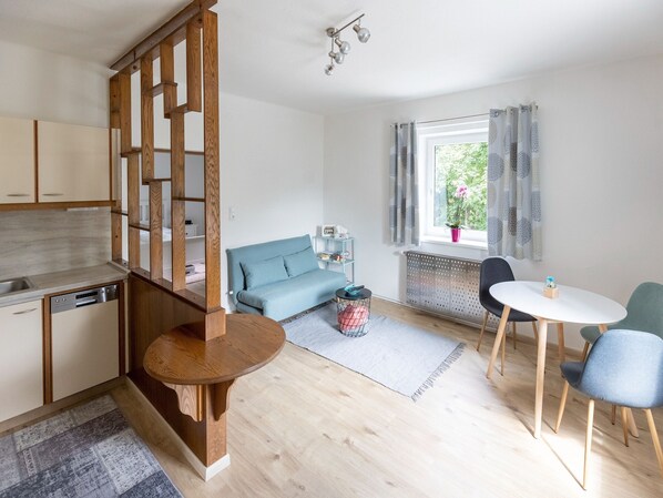 A modern kitchen with wooden cabinets, a built-in dishwasher, and a dining area with a round wooden table and two chairs. - Gailtaler Apartment at an Excursion Location (Kotschach-Mauthen)