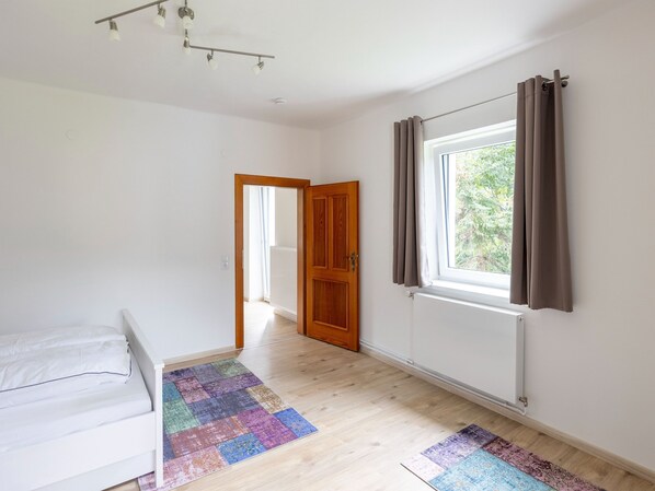 A bedroom with a bed, a colorful rug, a window with curtains, and a door leading to another room. - Gailtaler Apartment at an Excursion Location (Kotschach-Mauthen)