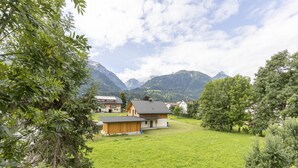 Ländliche Szene mit einem Haus, umgeben von einem üppigen grünen Feld und Bergen im Hintergrund.