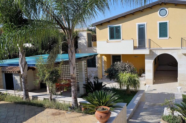 A two-story building with a yellow facade, a balcony, and a covered patio area. - Flat Near the sea With air Conditioning and Patio (Noto)