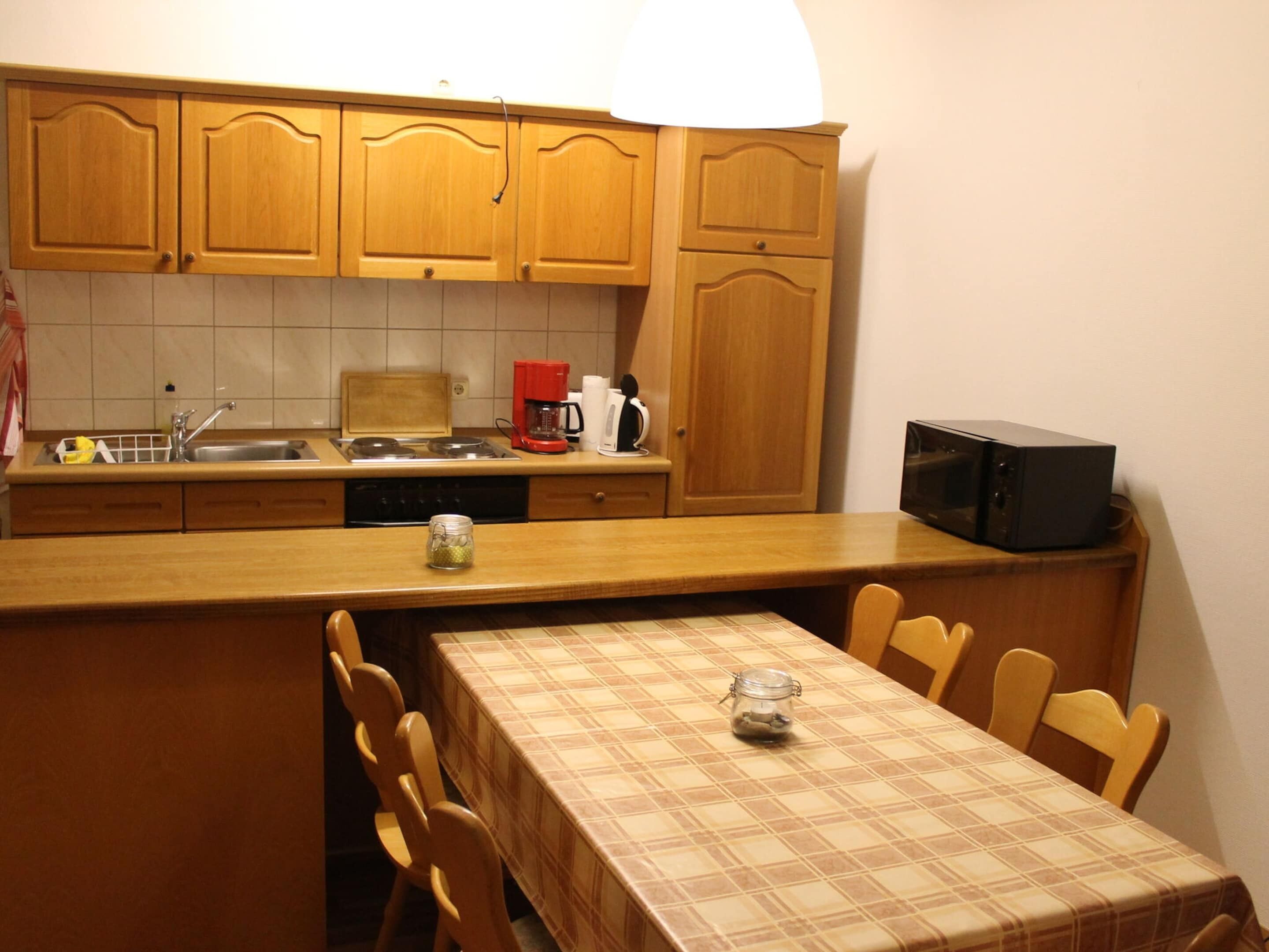 A small kitchen with wooden cabinets, a sink, a stove, a microwave, and a table with chairs.