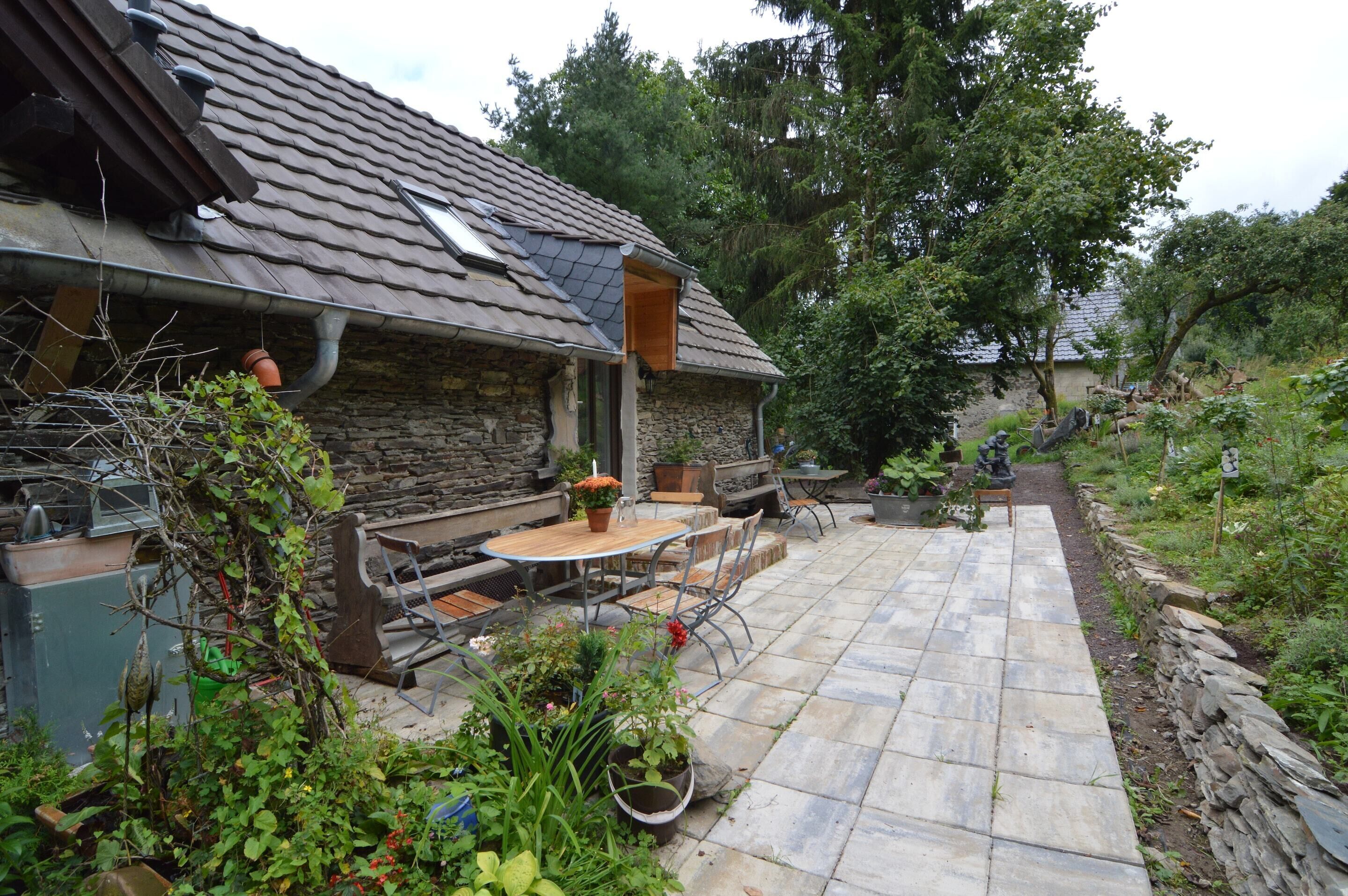 Una casa de piedra con patio de tejas, mobiliario exterior y jardín.