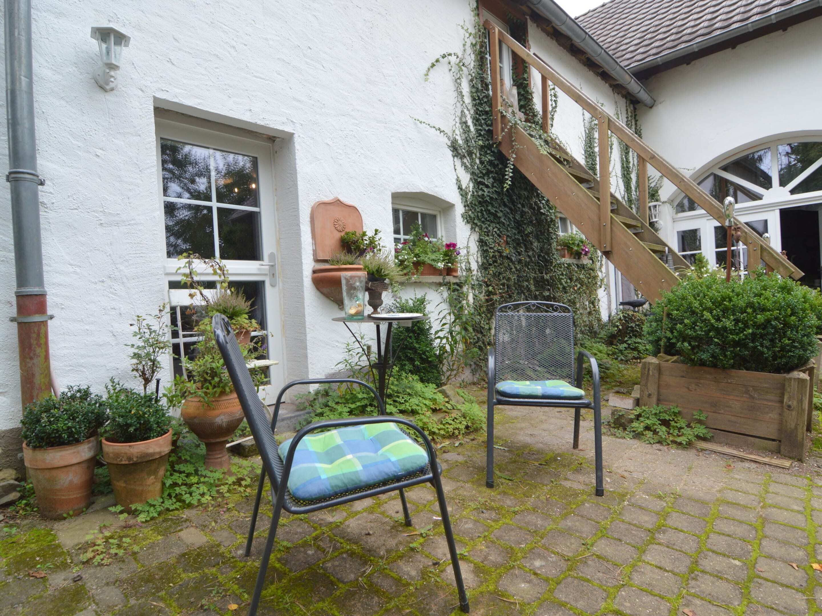 A courtyard with two metal chairs, a wooden staircase, and potted plants.