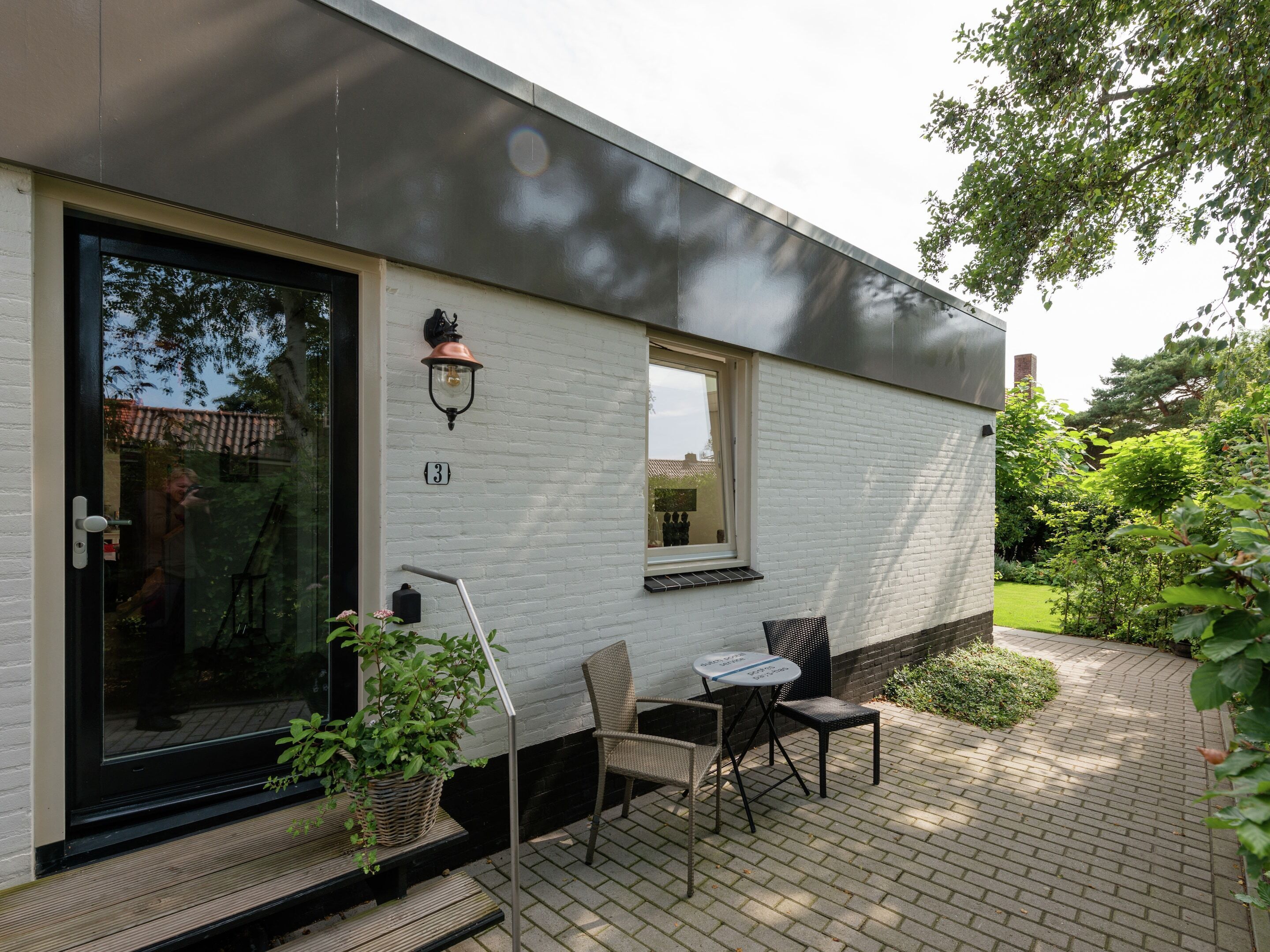 A modern house with a white exterior, a black door, and a small patio area with a table and chairs.