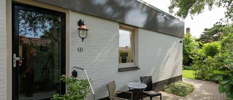 Et moderne hus med hvide vægge, en sort dør og en lille terrasse med et bord og stole.