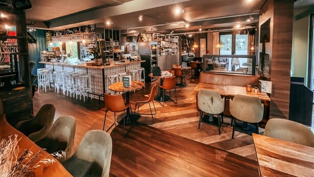 Un restaurant chaleureux avec un coin bar, un plancher en bois et différents types de sièges, notamment des tabourets de bar et des tables.