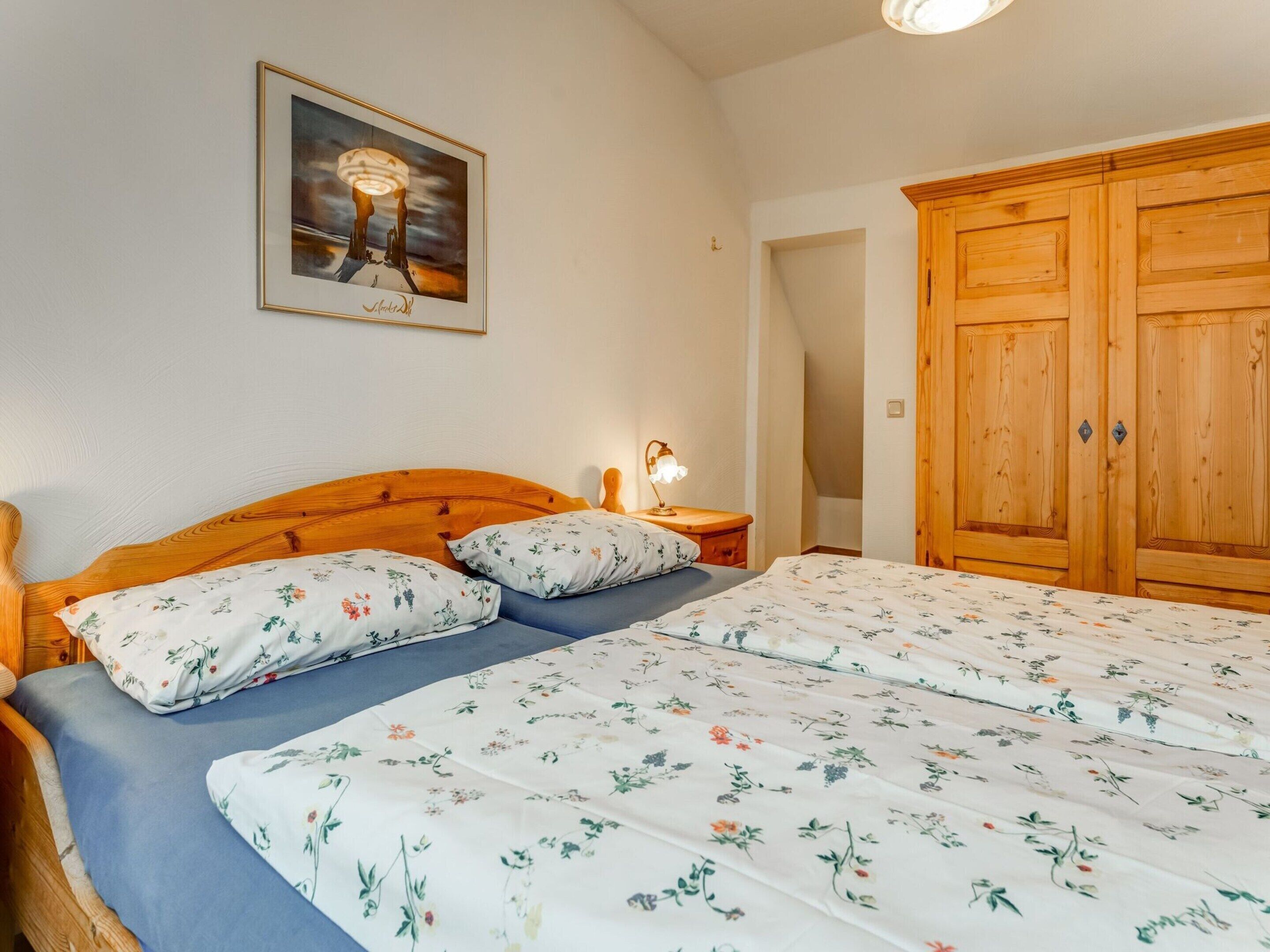 A bedroom with a wooden bed, floral bedding, a nightstand with a lamp, and a wooden wardrobe.