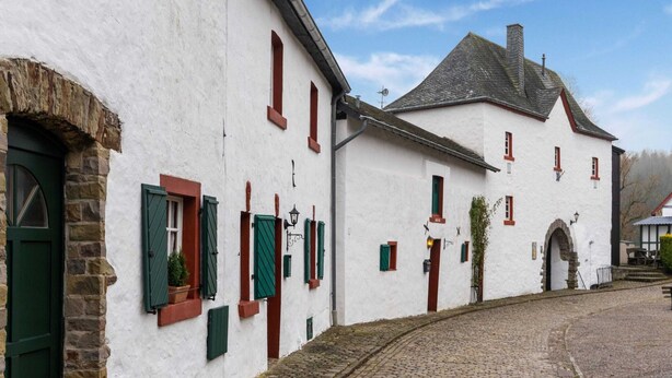 Um edifício tradicional branco com portadas verdes, uma rua de paralelepípedos e um arco de pedra.