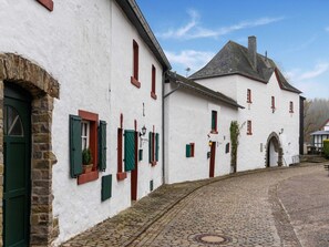 Ein traditionelles weißes Gebäude mit grünen Fensterläden, eine Kopfsteinpflasterstraße und ein Steinbogen.