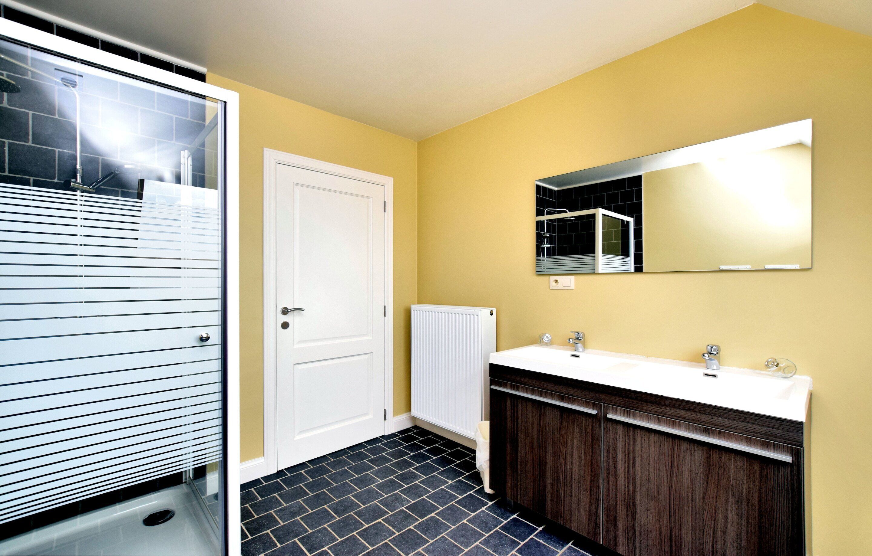 Un baño con una puerta blanca, un espejo grande, un lavabo blanco y armarios de madera oscura.