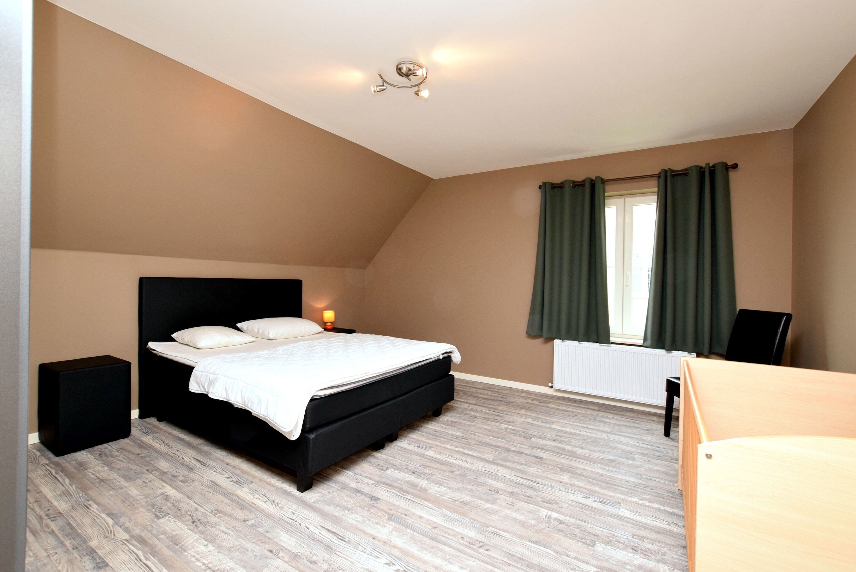 A bedroom with a bed, bedside tables, a window with curtains, and a radiator.