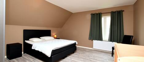 A bedroom with a bed, bedside tables, a window with curtains, and a radiator.