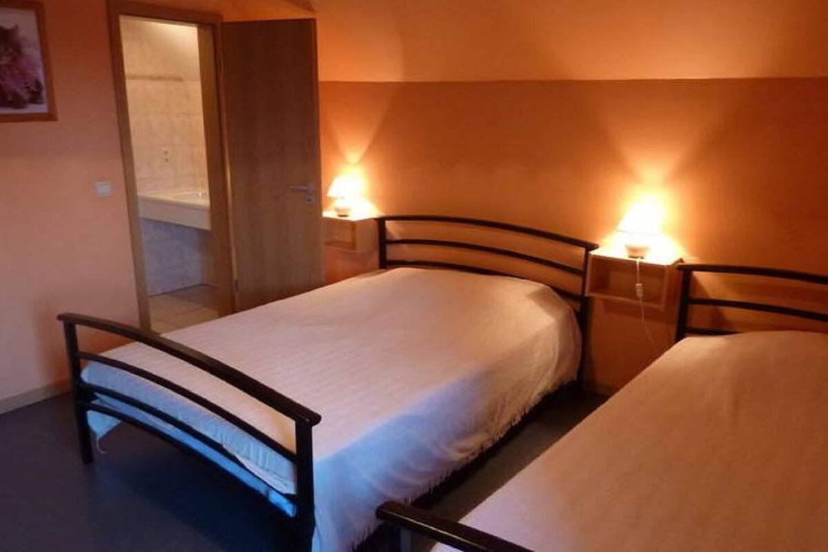 A small, cozy bedroom with two single beds, a wooden door, and a bathroom visible through an open door.