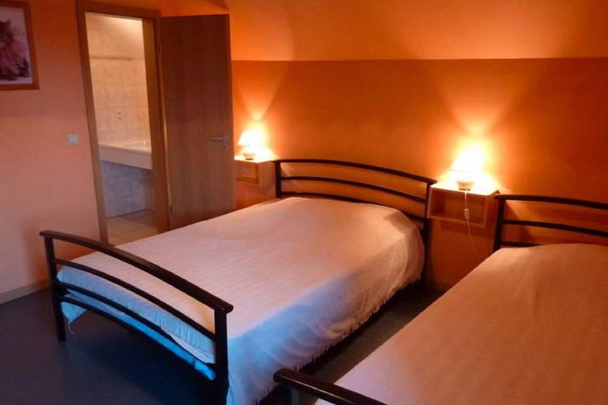 A single bed with a wooden frame and a white mattress in a room with orange walls. There are two bedside tables with lamps.