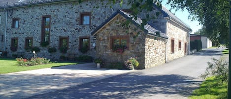 A stone building with a sloped roof, a paved driveway, and a small garden with flowers.