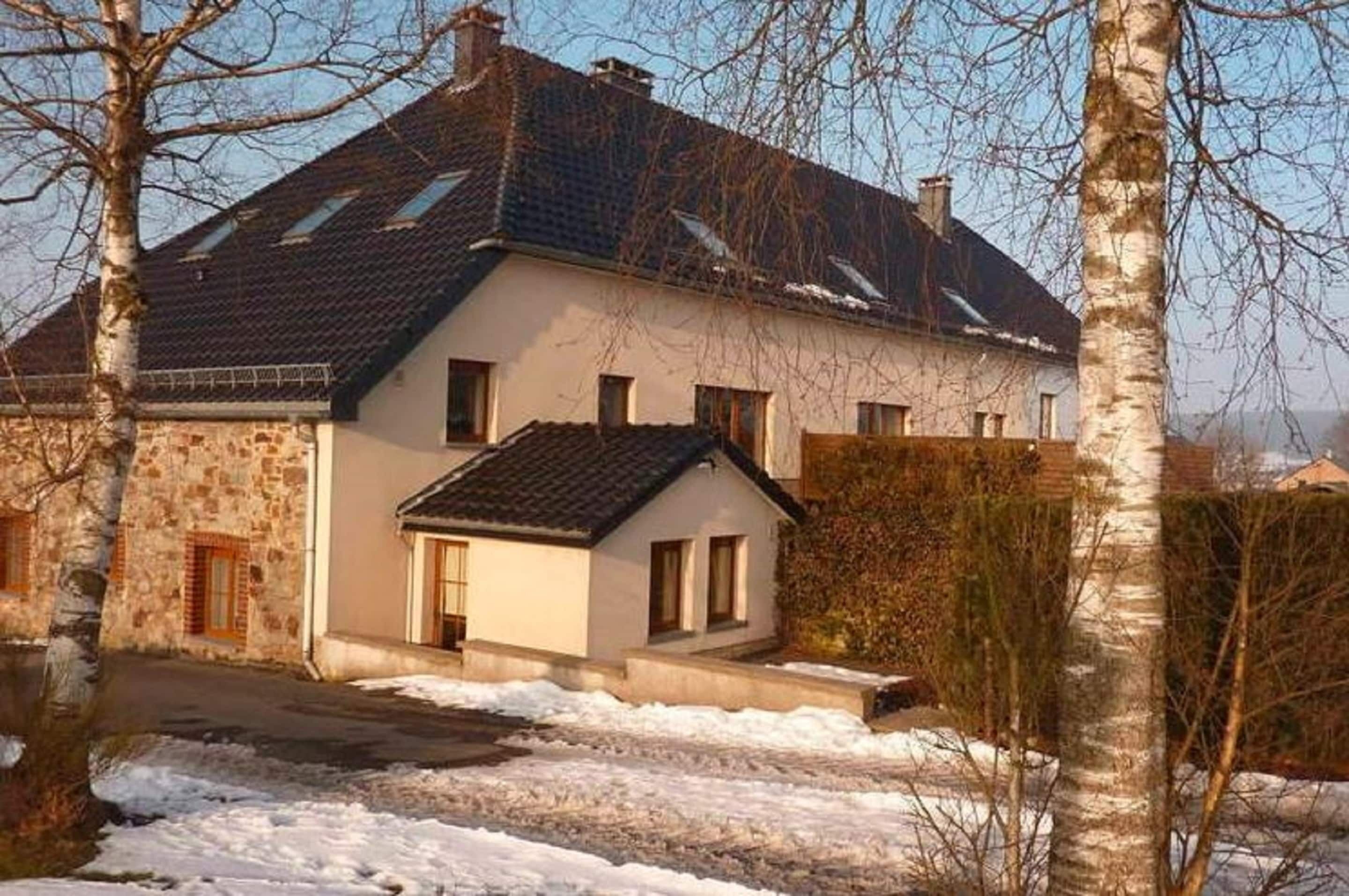A two-story house with a stone facade and a tiled roof, surrounded by bare trees and a snow-covered ground.