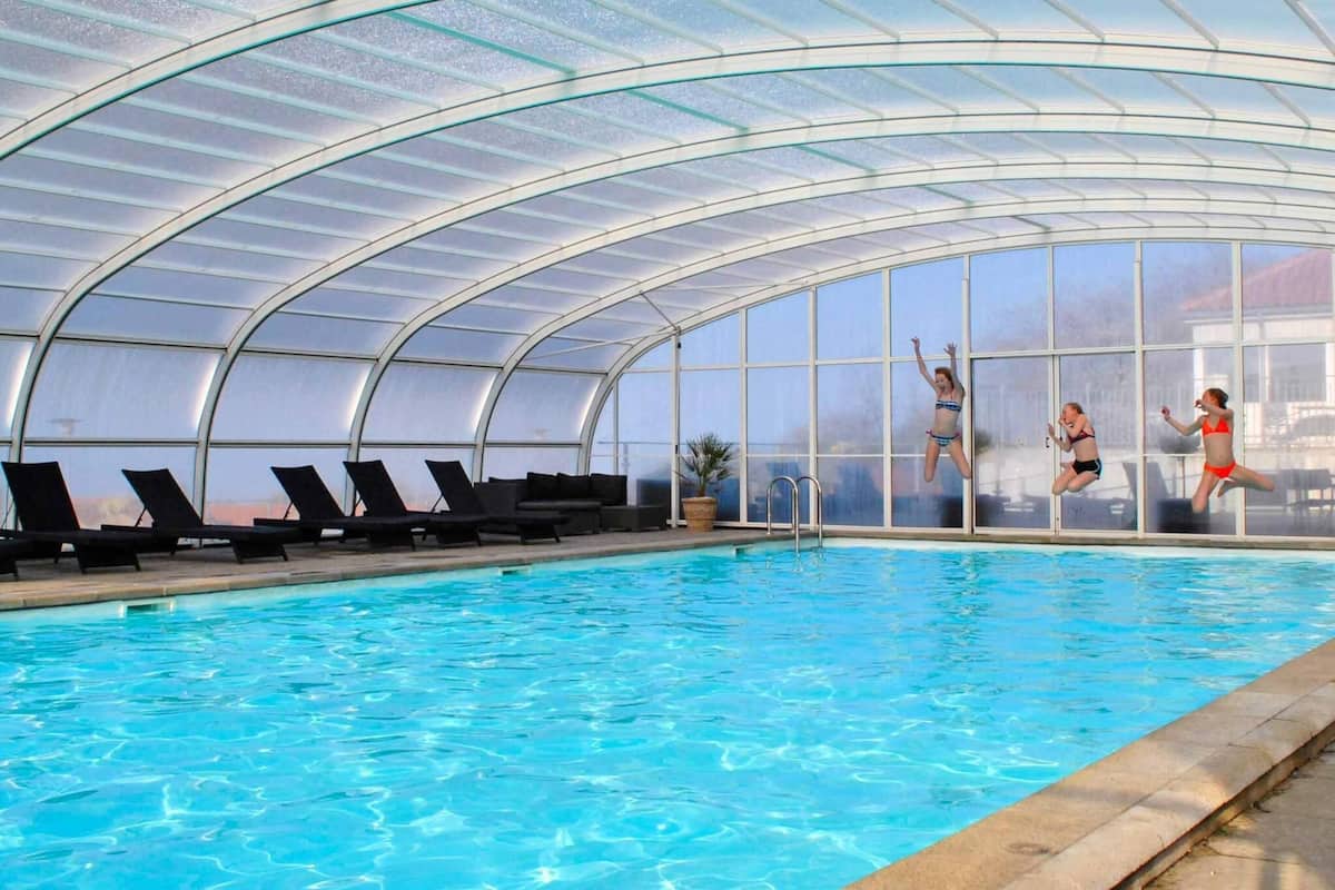 Une piscine intérieure avec des parois en verre transparent, des chaises longues et un escalier pour accéder à la piscine.