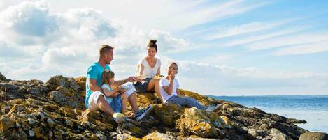 A family of four sitting on rocky terrain with a view of the sea.