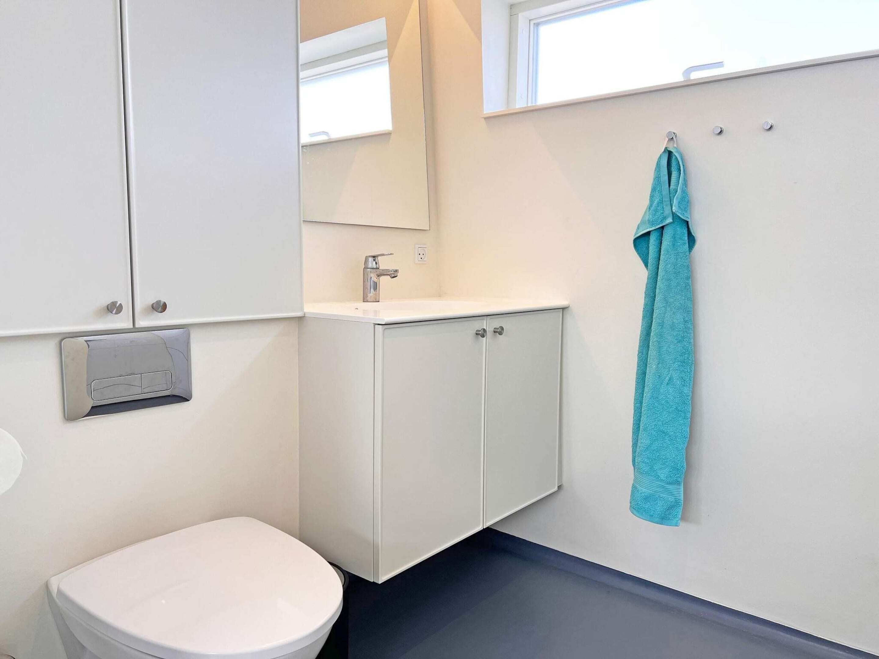 A bathroom with a white toilet, a sink with a mirror above it, and a towel hanging on a rack.