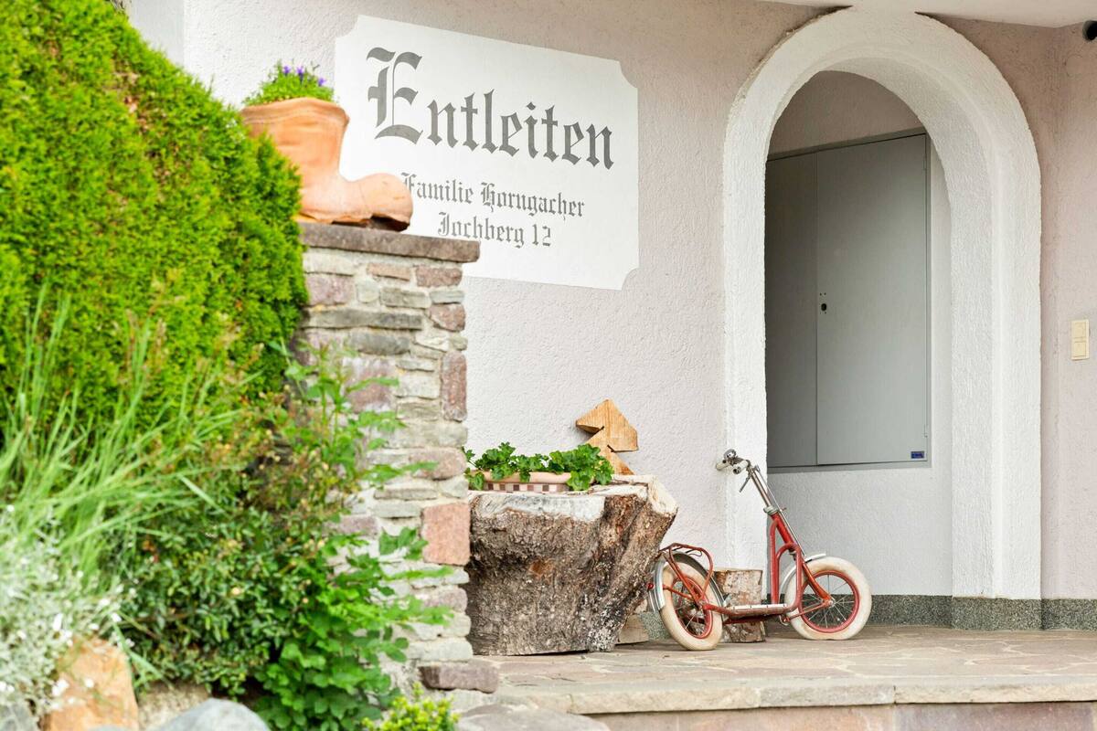 Entrada de un edificio con un cartel que dice 'Entleiten' y una bicicleta estacionada afuera.