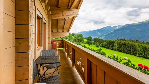 A wooden balcony with a table and chairs, overlooking a green valley and mountains. - Sunlit Apartment Near Ski Area in Hollersbach im Pinzgau (Hollersbach im Pinzgau)