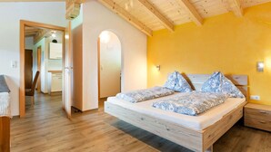 A bedroom with a wooden ceiling, a bed with patterned bedding, a bedside table, and a small drawer unit. - Sunlit Apartment Near Ski Area in Hollersbach im Pinzgau (Hollersbach im Pinzgau)