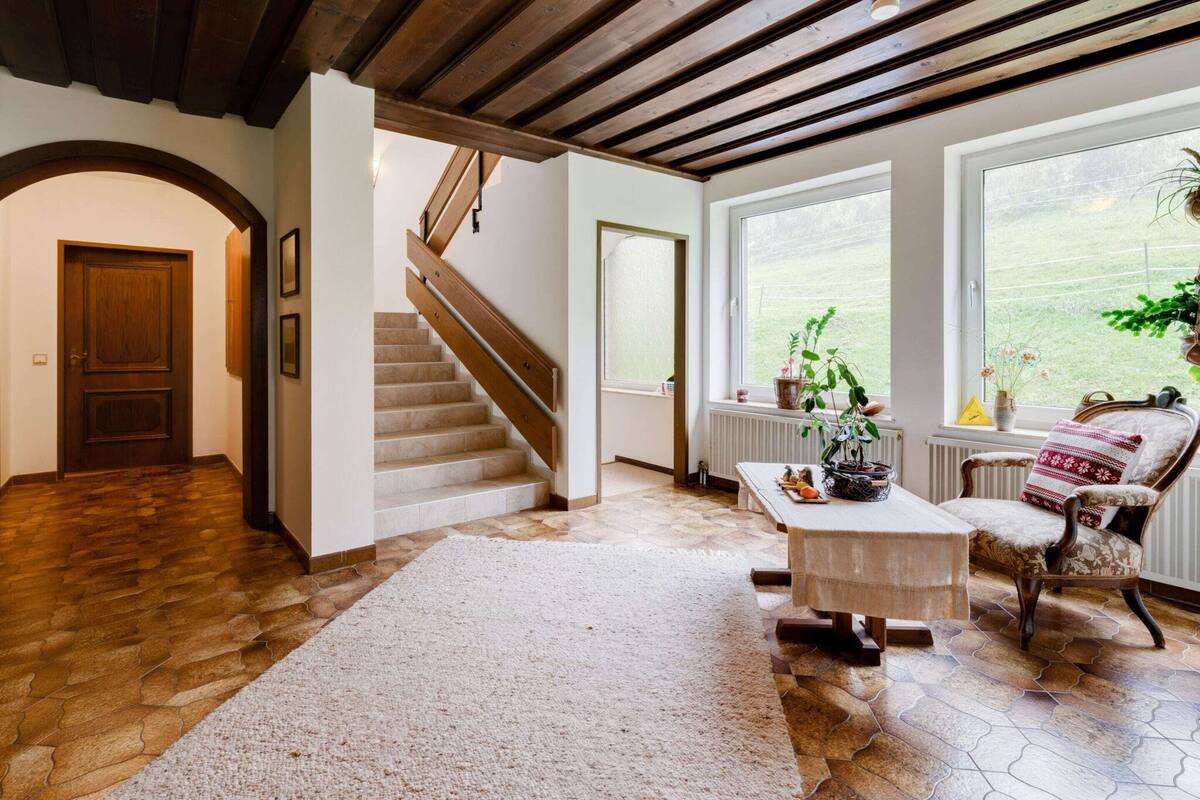 Une pièce spacieuse avec un escalier en bois, une grande fenêtre offrant une belle vue et un coin salon confortable avec un fauteuil et une table.