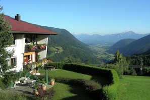A house with a red roof, a balcony with flowers, and a view of mountains.