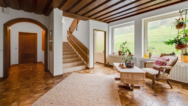 Un vaste espace de vie agrémenté d’un escalier en bois, d’une grande fenêtre offrant une vue sur l’extérieur et d’un coin salon confortable avec un fauteuil à motifs et une petite table.