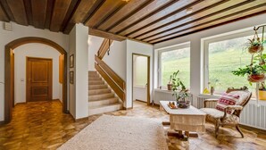 Un vaste espace de vie agrémenté d’un escalier en bois, d’une grande fenêtre offrant une vue sur l’extérieur et d’un coin salon confortable avec un tapis à motifs.