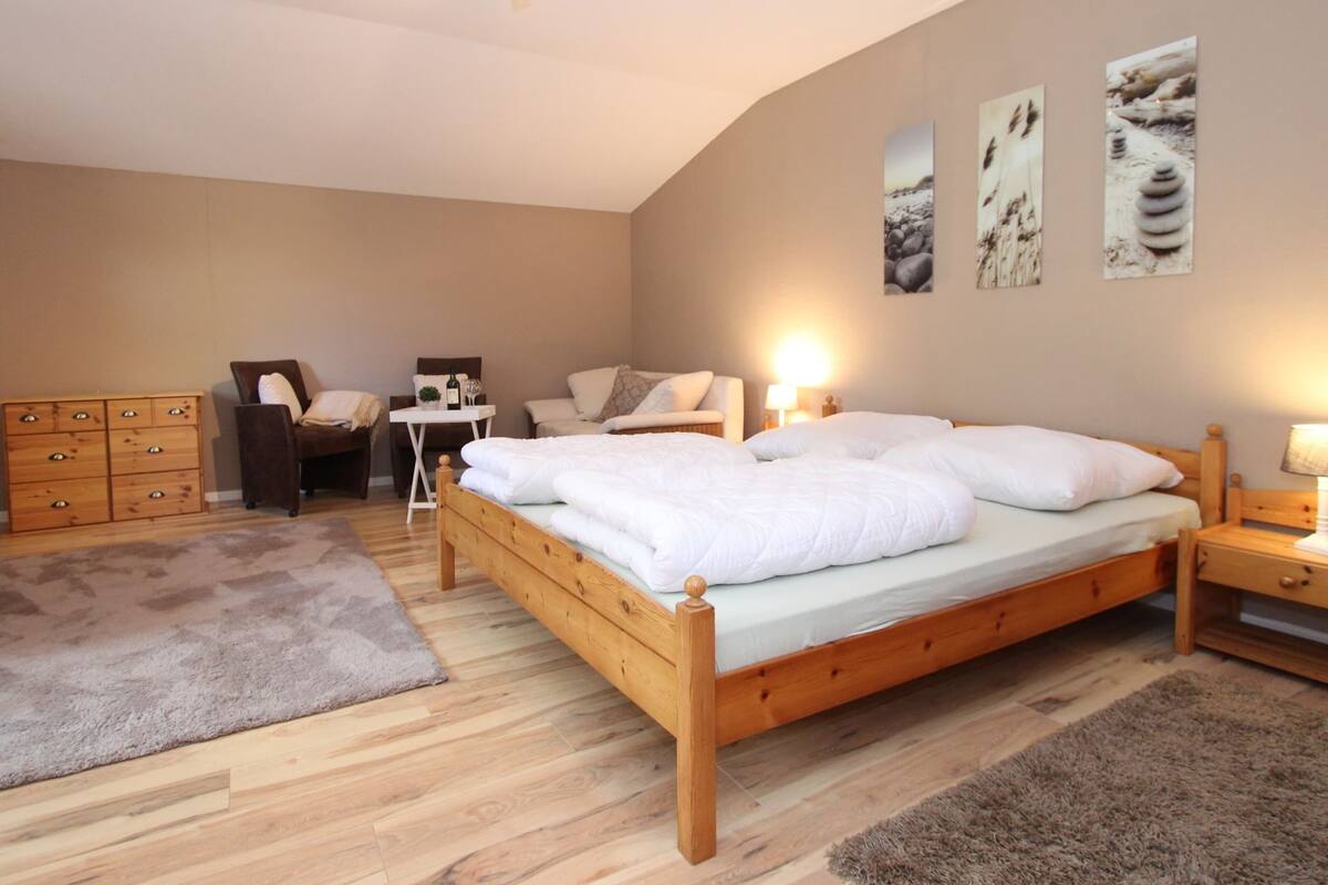 Ein Schlafzimmer mit einem hölzernen Bett, einem Schreibtisch, einem Stuhl, einer Kommode und Wandbildern.