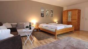 A bedroom with a wooden bed, a white sofa, a small table with a bottle, and a wooden wardrobe. - Holiday Home in Kirchdorf With Swimming Pool,terrace, Garden (Kirchdorf)