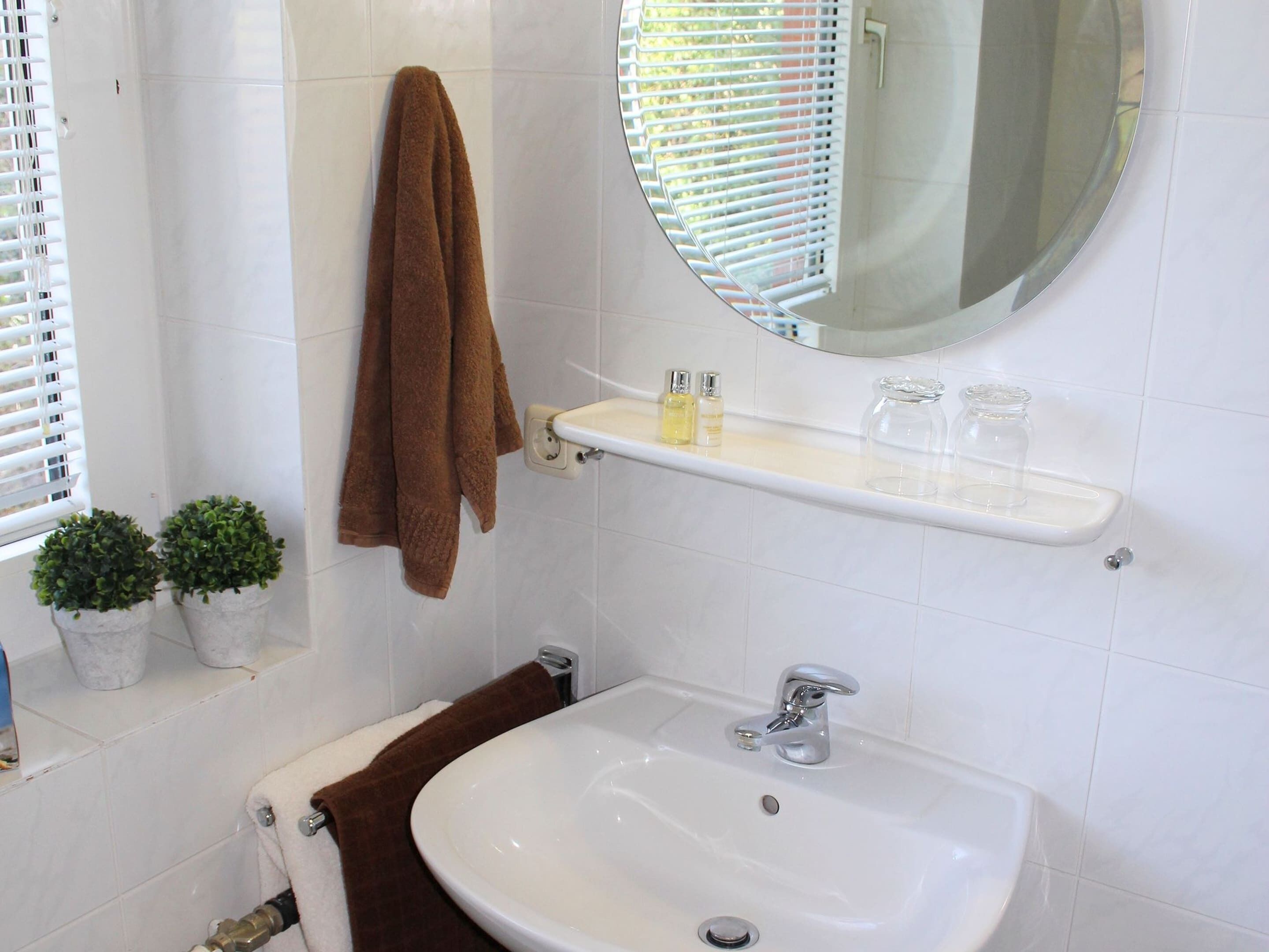 A bathroom with a white sink, a mirror, a towel rack, and two potted plants.