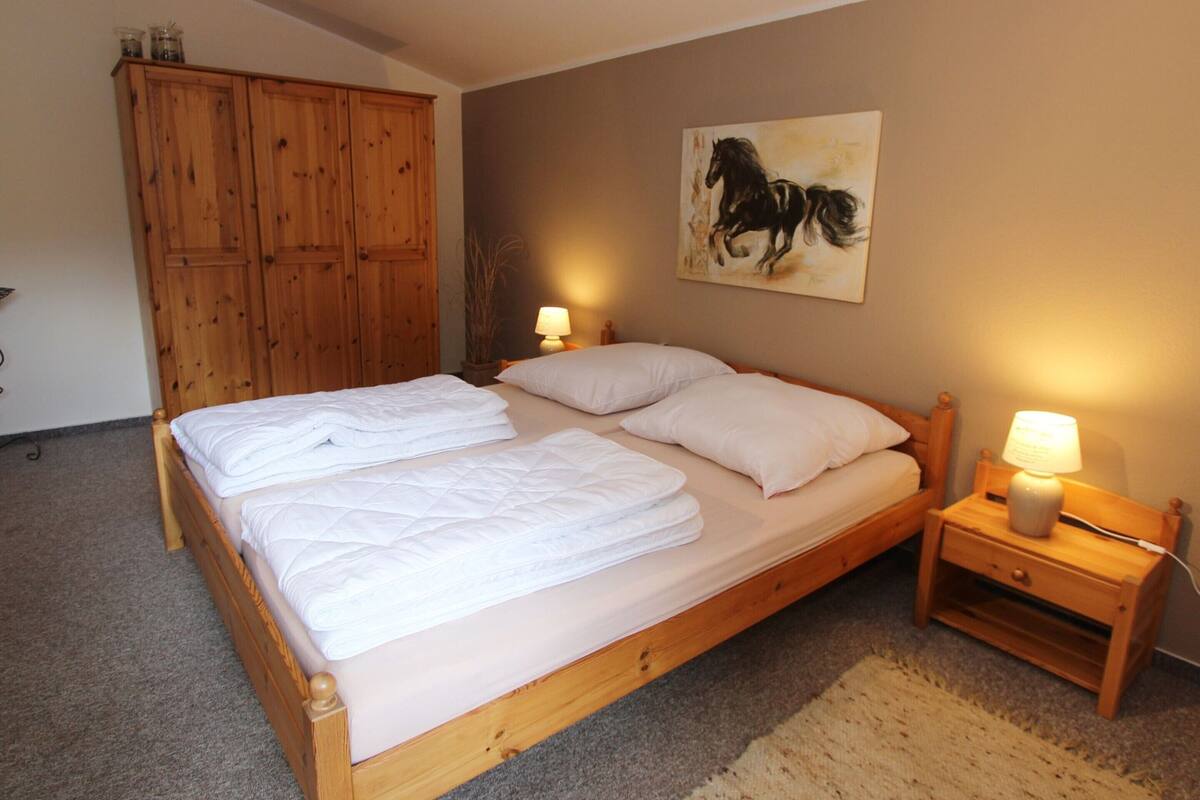 Ein Schlafzimmer mit einem hölzernen Bett, zwei Nachttischen mit Lampen, einem Holzschrank und einem Gemälde von einem Pferd an der Wand.