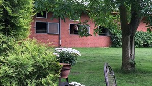 A brick building with windows, a tree, and a metal chair in a grassy area. - Holiday Home in Kirchdorf With Swimming Pool,terrace, Garden (Kirchdorf)