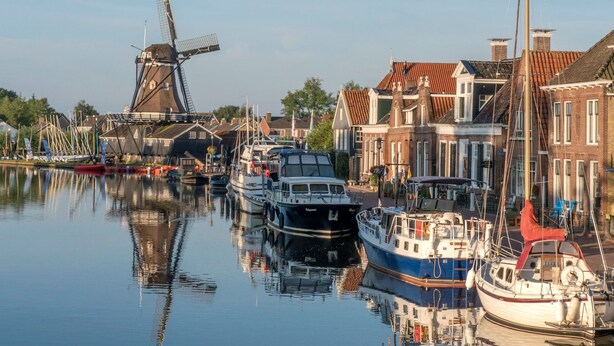 A canal with boats docked, a windmill, and traditional buildings. - Secluded Chalet in Suwald With Hottub (Suwâld)