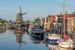 Een gracht met afgemeerde boten, een windmolen en traditionele gebouwen.