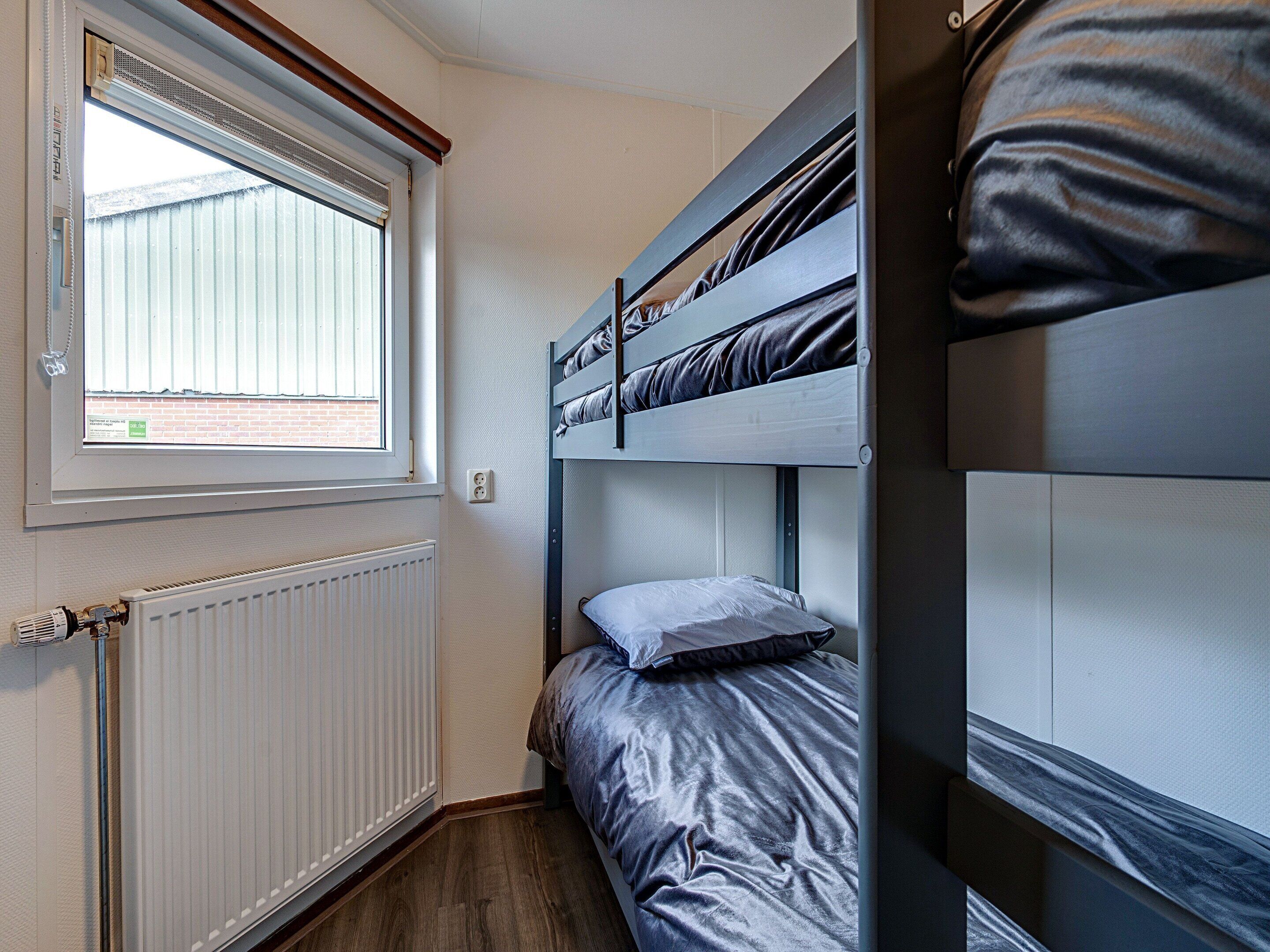 A bunk bed room with a window, radiator, and wooden floor.