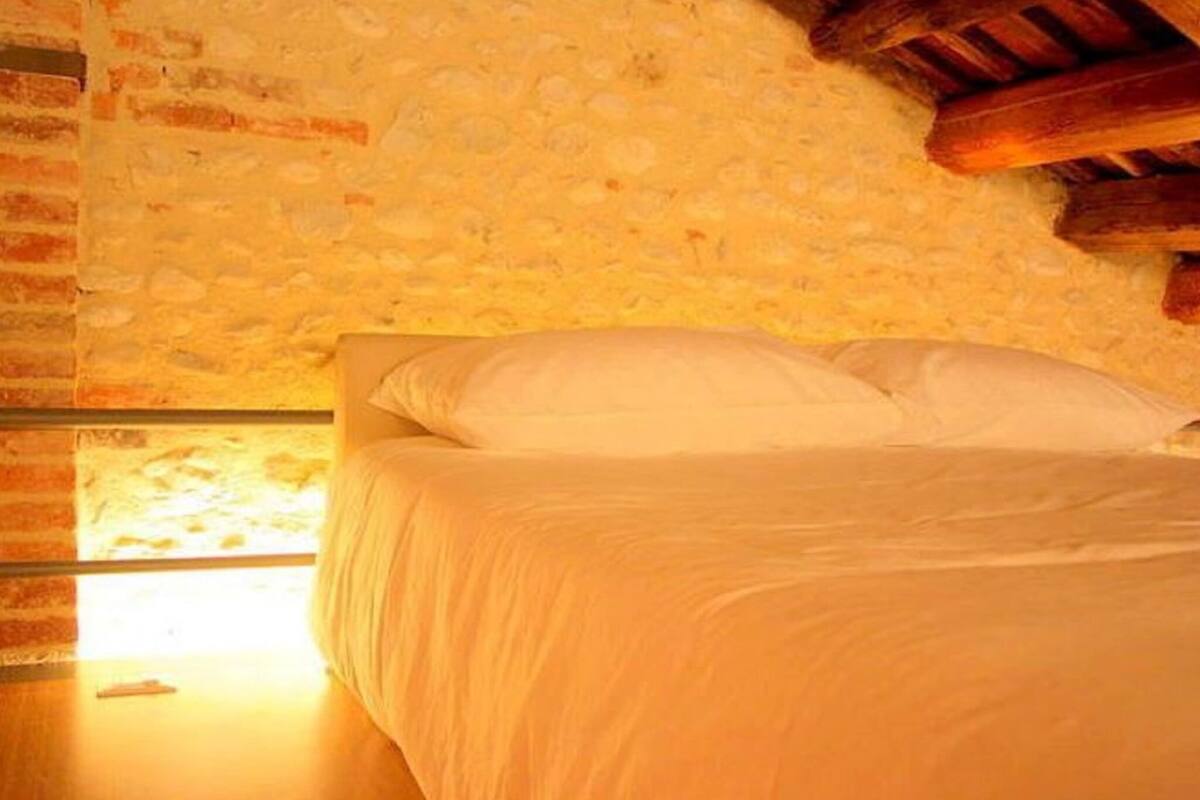 A bedroom with a stone wall, a wooden ceiling, and a bed with white bedding.