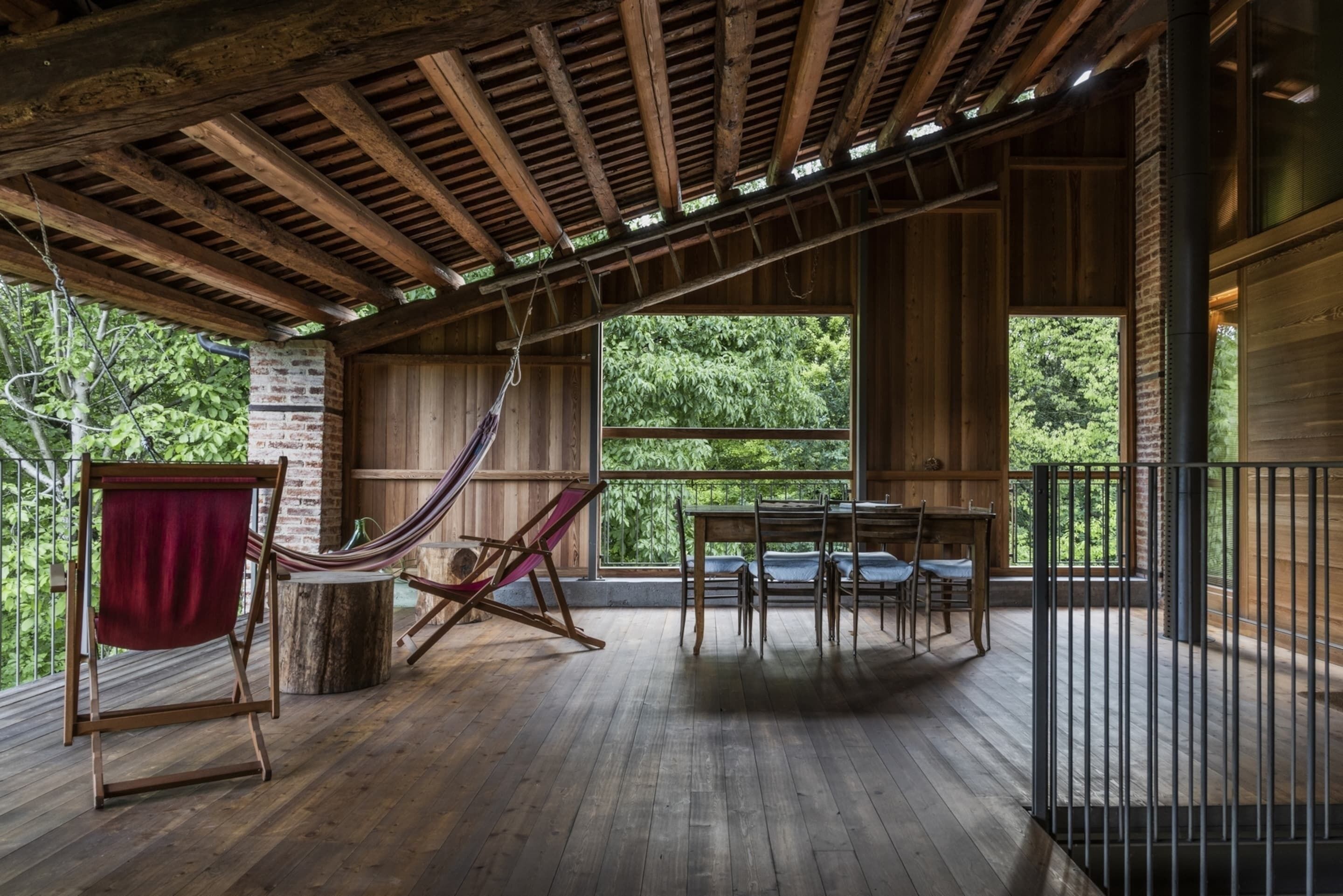 Une terrasse en bois avec un hamac, une table et des chaises, offrant une vue sur un paysage verdoyant et luxuriant.