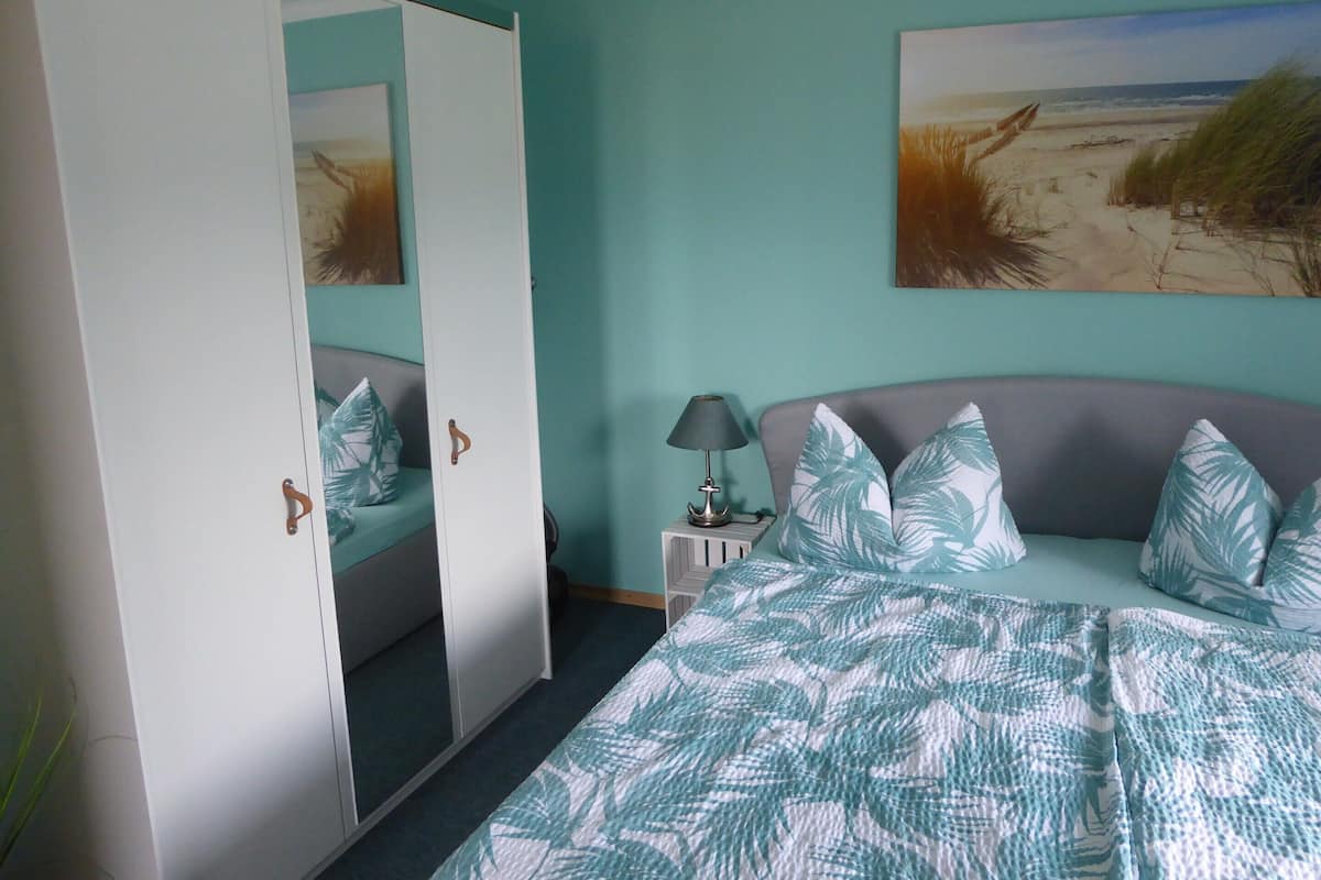 Ein Schlafzimmer mit Bett, Kleiderschrank, Nachttisch und einem Wandbild mit Strandmotiv.