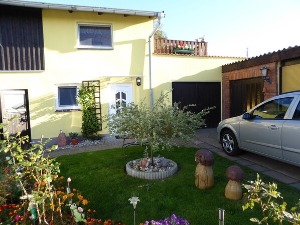 Un edificio residenziale con garage, un'auto parcheggiata di fronte e un giardino curato con diverse piante e una statua decorativa a forma di coniglio.
