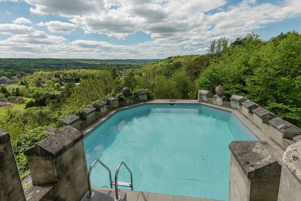 A rectangular pool with a stone border, surrounded by lush greenery and a clear sky.