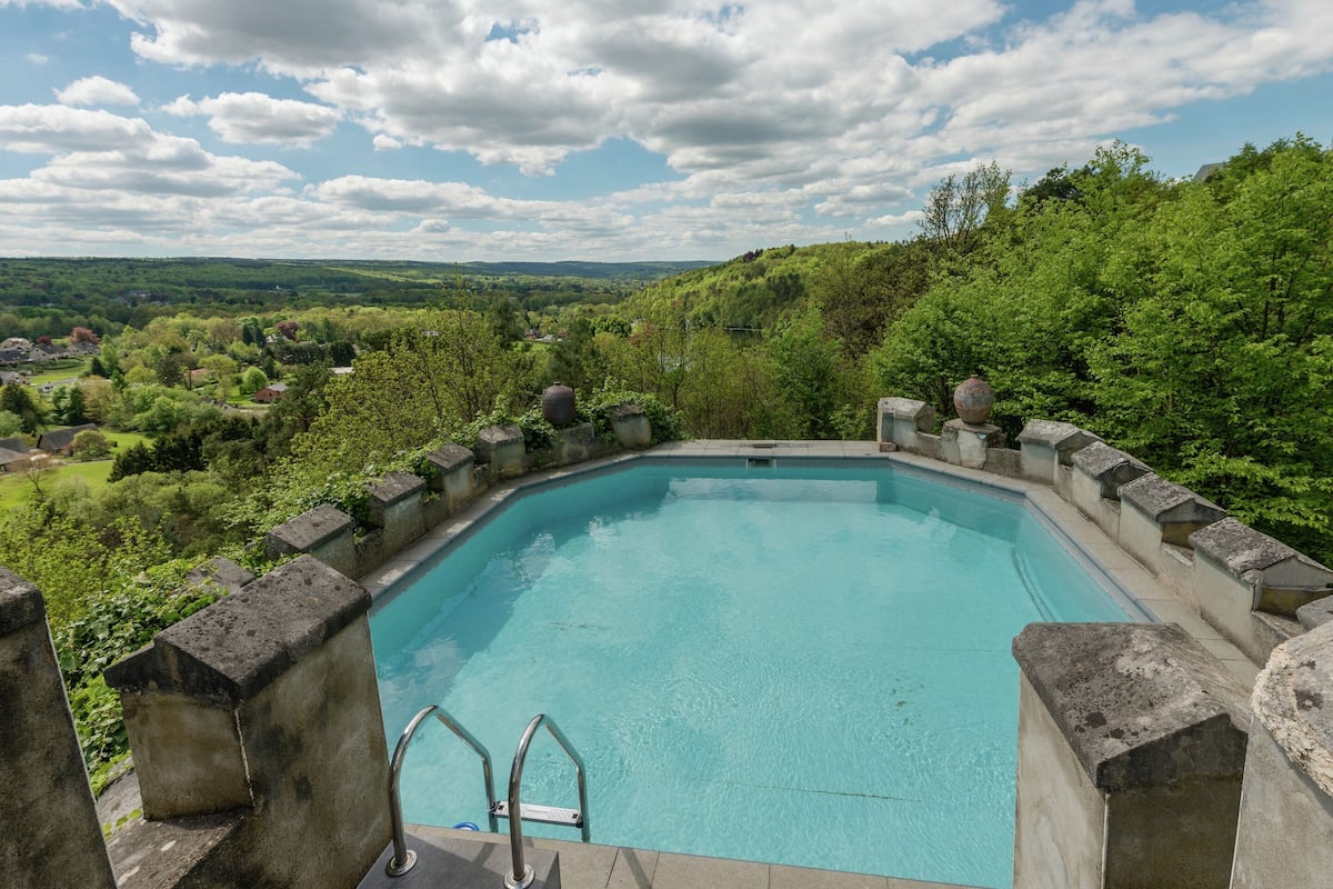 A rectangular pool with a stone border, surrounded by lush greenery and a clear sky.