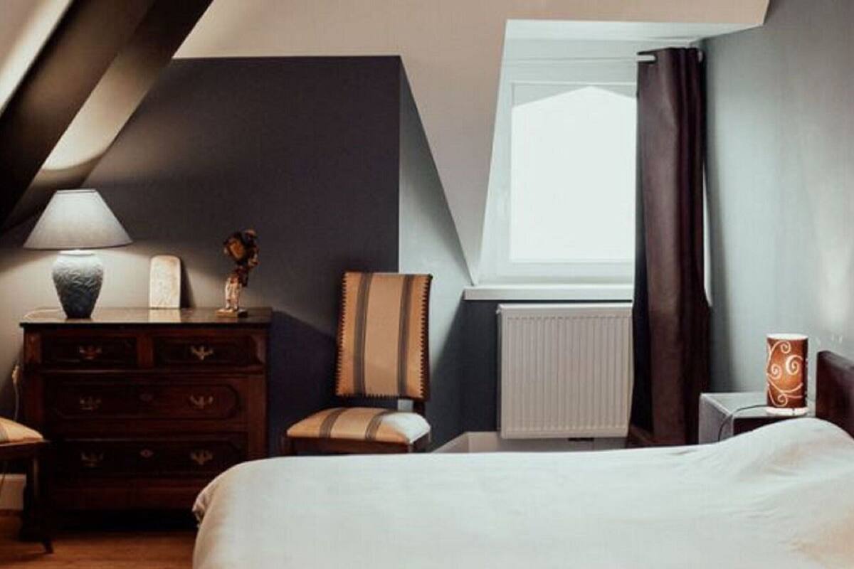 Un dormitorio con cama, cómoda, lámpara, ventana con cortinas y radiador.