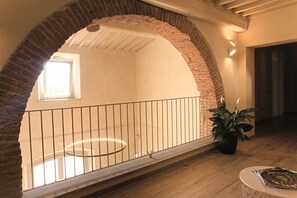 An interior view of a room with a brick archway, a balcony with a metal railing, a potted plant, and a round table with a magazine. - Modern Apartment in Agliana With Shared Garden (Agliana)