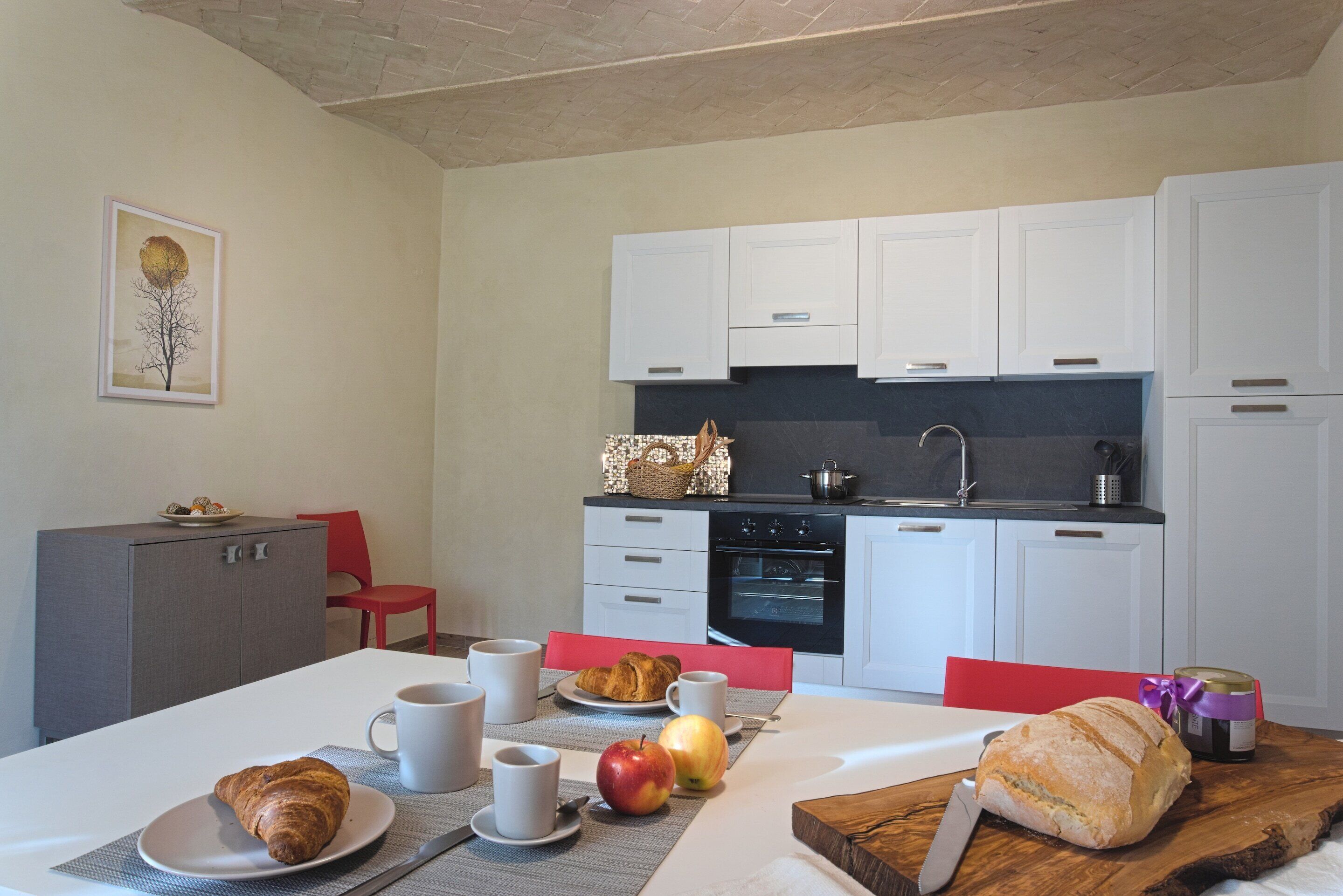 Un coin repas avec une table mise pour le petit-déjeuner, comprenant des croissants, des fruits et une miche de pain.