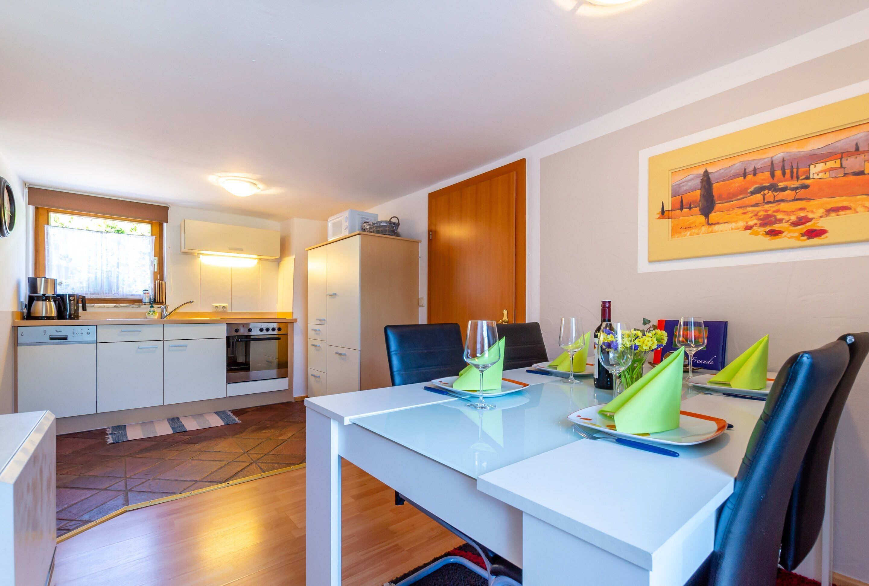A modern kitchen with white cabinetry, a built-in oven, and a dining area with a white table set for two.