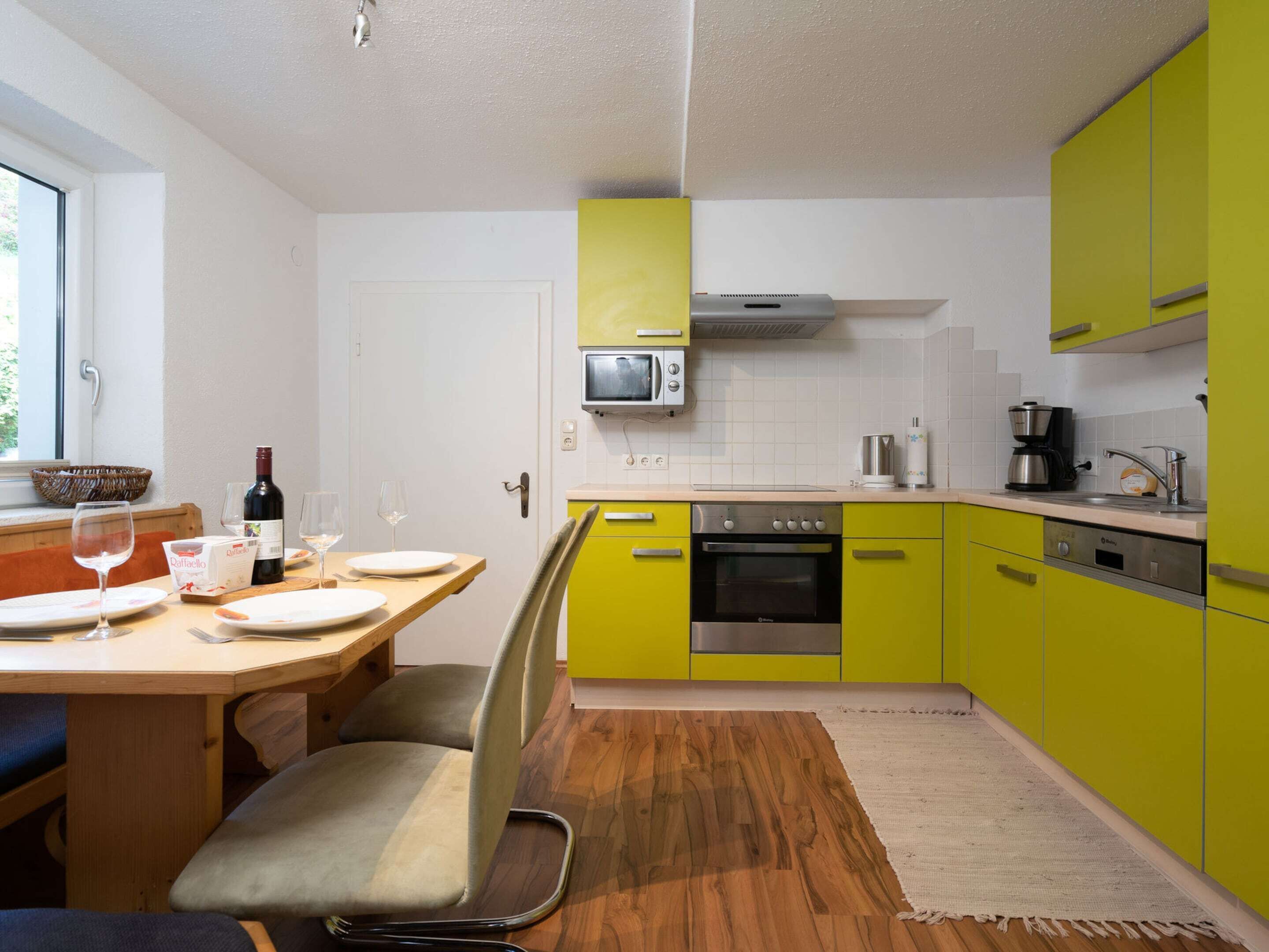 A modern kitchen with yellow cabinets, a wooden dining table, and a built-in oven.